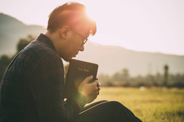 Image of a man holding a Bible and praying in nature
